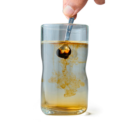 Glass of amber liquid with a spoon stirring it, on a white background