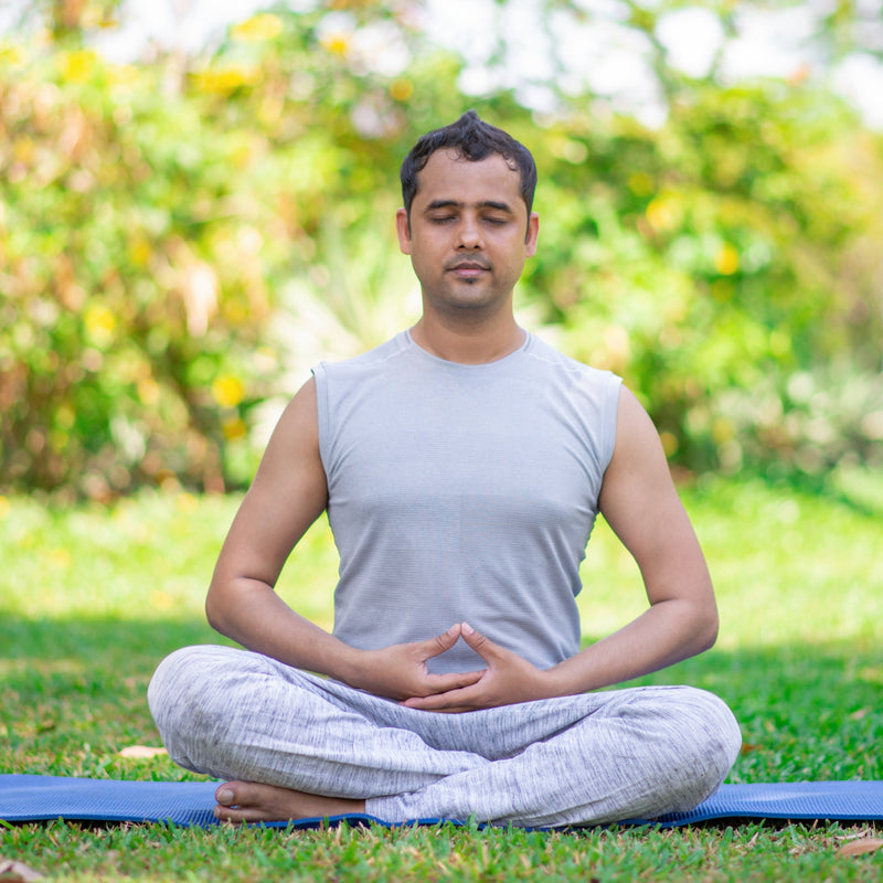 Man meditating on a yoga mat in a park with greenery